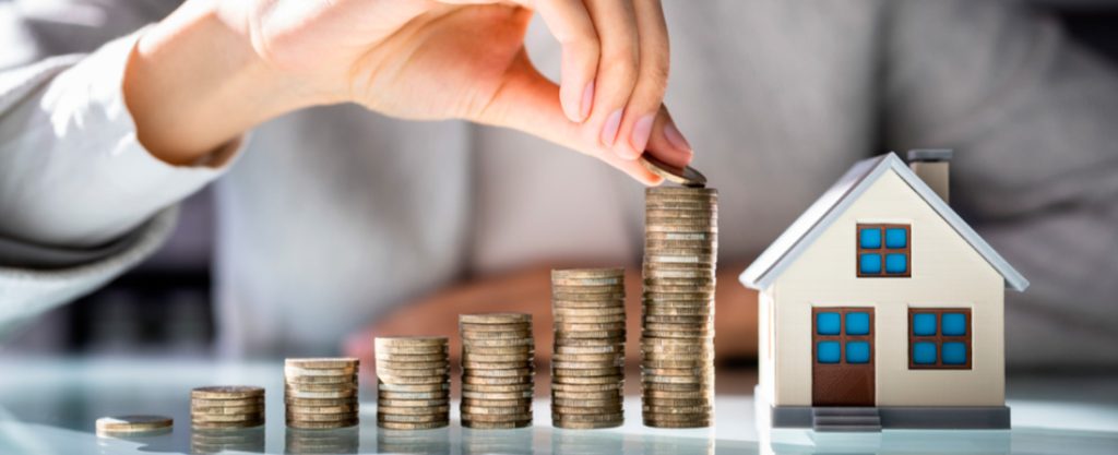 Persona apilando monedas al lado de la maqueta de una casa